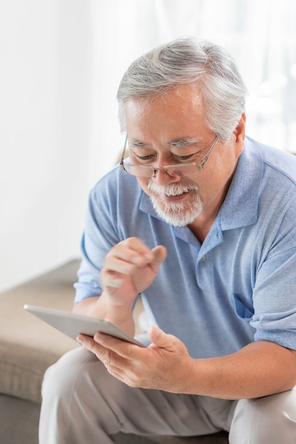 Älterer asiatischer Mann, der ein Smartphone verwendet, lächelt glücklich auf dem Sofa zu Hause - Lifestyle-Konzept für ältere ältere Menschen