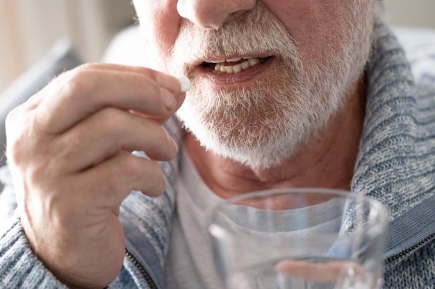 Älterer bärtiger mann, der eine pille mit einem glas wasser nimmt gesundheitsversorgung und personenkonzept