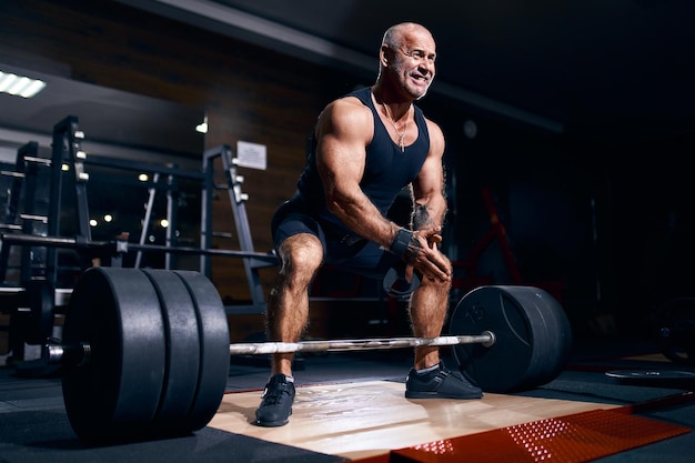 Älterer Bodybuilder, der sich darauf vorbereitet, Kreuzheben mit Langhantel zu trainieren, während er in einem Fitnessstudio Crosstraining macht