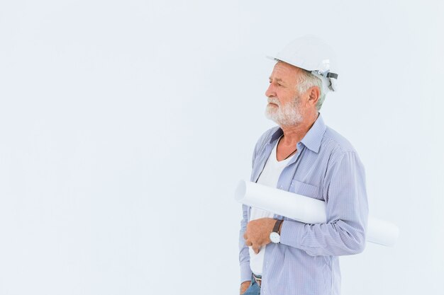 Älterer ernster Bauingenieur mit Schutzhelm mit Papierrollenplan im Studio mit Leerraum für Text