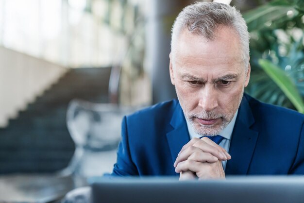 Älterer Geschäftsmann, der am Laptop arbeitet, während er in der Lobby sitzt