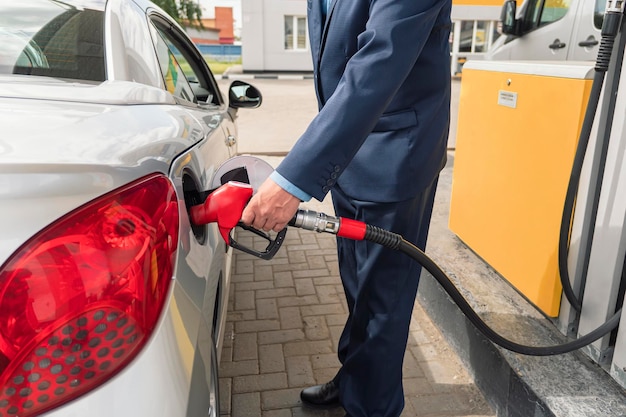 Älterer Geschäftsmann, der auf Tankstelle steht und Auto betankt