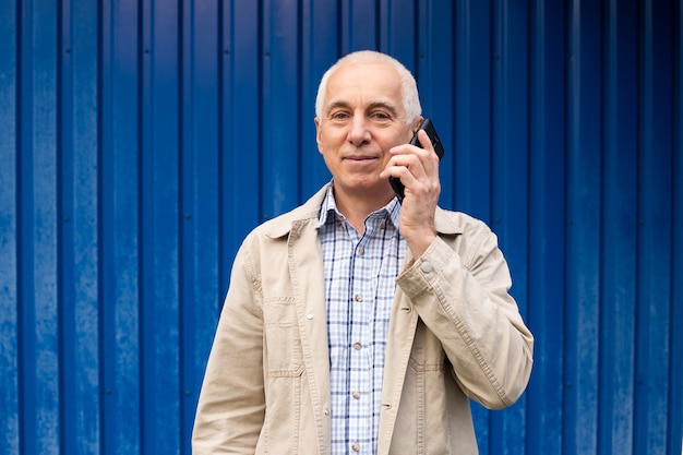 Älterer Geschäftsmann, der ein Gespräch am Telefon auf blauem Hintergrund hat