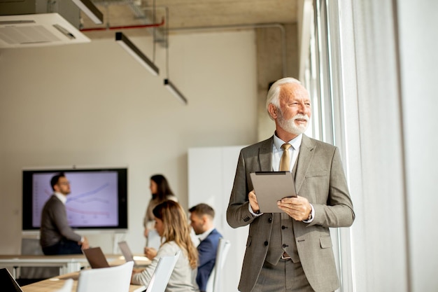 Älterer Geschäftsmann, der im Büro an einem digitalen Tablet arbeitet