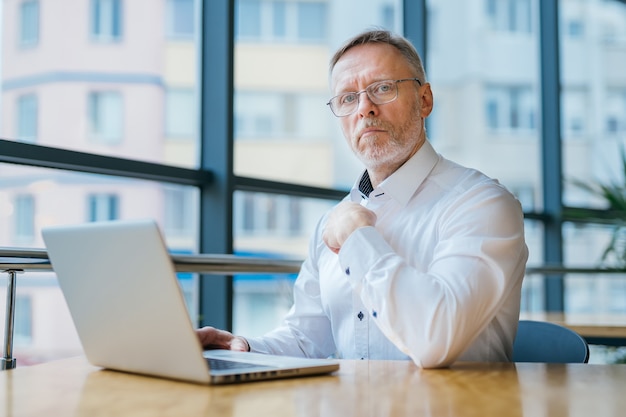 Älterer Geschäftsmann, der Kamera betrachtet. Älterer Mann, der mit Laptop arbeitet. Hübscher Geschäftsmann mittleren Alters.