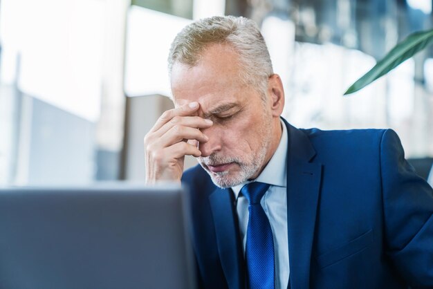 Älterer Geschäftsmann fühlt sich gestresst, während er in der Bürolobby am Laptop arbeitet