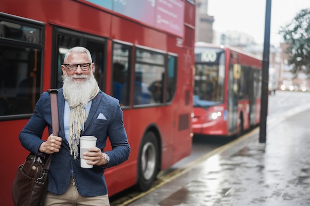 Älterer Geschäftsmann geht zur Arbeit und trinkt Kaffee mit Londoner Busbahnhof im Hintergrund - Fokus auf Gesicht