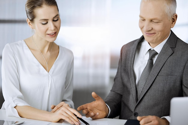 Älterer Geschäftsmann und Frau sitzen und kommunizieren im sonnigen Büro. Erwachsene Geschäftsleute oder Anwälte, die bei Treffen als Partner und Kollegen zusammenarbeiten.