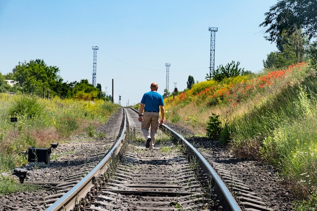 Älterer Glatzkopf geht in die Ferne entlang der Eisenbahnschienen