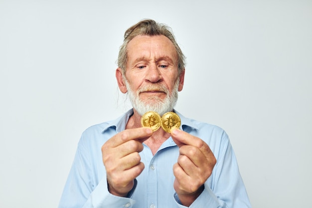 Älterer grauhaariger mann finanziert goldmünzen bitcoin nahe hellem hintergrund des gesichtes