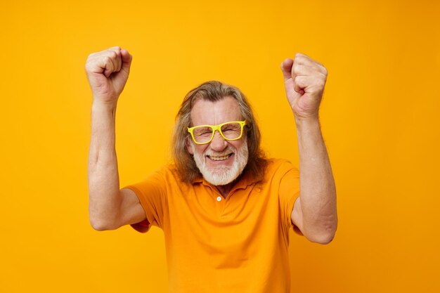 Älterer grauhaariger Mann, gelbes T-Shirt und Brille, die gelben Hintergrund posieren