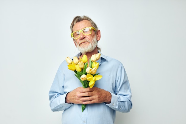 Älterer grauhaariger Mann in einem blauen Hemd mit einem Blumenstrauß auf hellem Hintergrund