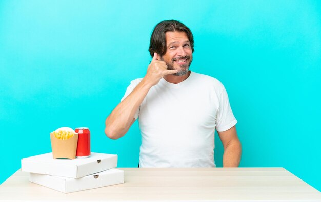 Älterer holländischer Mann, der Fast Food isst, sitzt an einem Tisch und macht eine Telefongeste