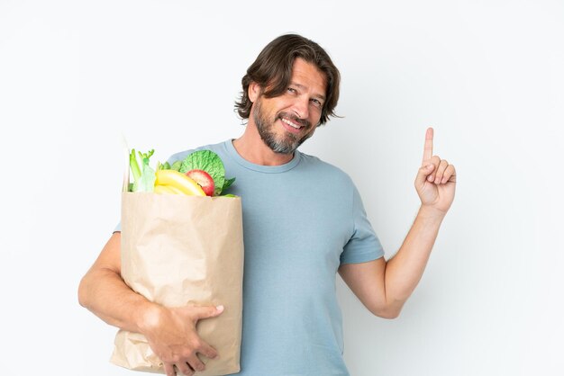Älterer holländischer Mann, der Lebensmitteleinkaufstasche über isoliertem Hintergrund hält und einen Finger im Zeichen der Besten zeigt und hebt