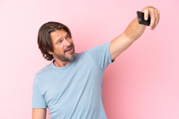 Älterer holländischer Mann isoliert auf rosa Hintergrund, der ein Selfie mit Handy macht