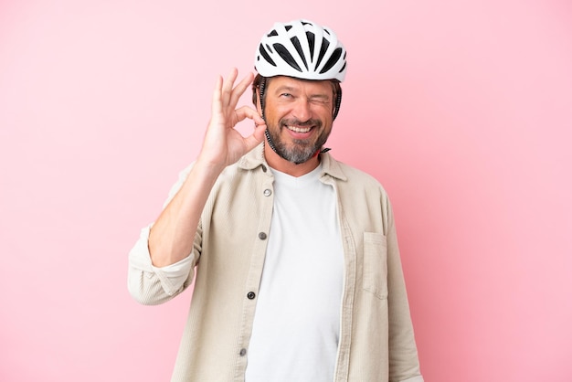 Älterer holländischer Mann mit Fahrradhelm isoliert auf rosafarbenem Hintergrund, der mit den Fingern ein Ok-Zeichen zeigt
