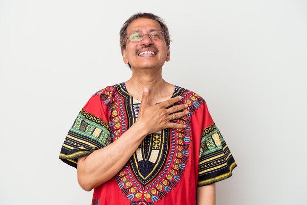 Älterer indischer Mann, der ein indisches Kostüm einzeln auf weißem Hintergrund trägt, lacht laut und hält die Hand auf der Brust.