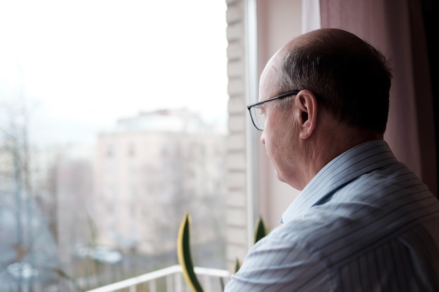 Älterer kaukasischer Mann, der mit einsamem Ausdruck aus dem Fenster schaut