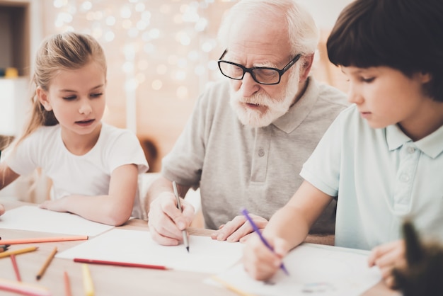 Älterer Künstler bringt Enkelkindern das Zeichnen bei.