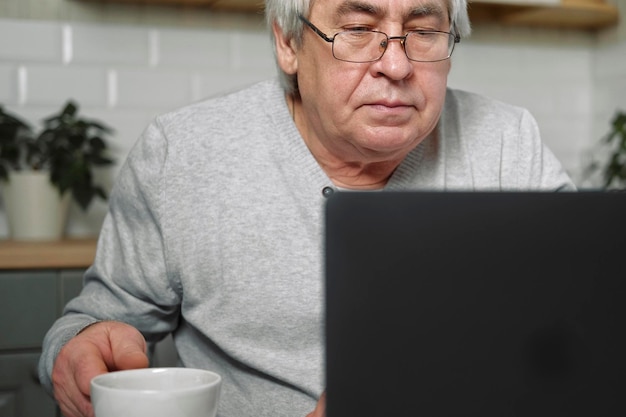 Älterer männlicher Geschäftsinhaber mit Brille, der am Schreibtisch vor dem Laptop sitzt. Erfolgreicher älterer Mann, der zu Hause arbeitet. Grauhaarige 60er 70er Jahre