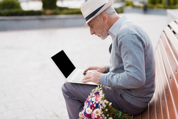 Älterer Mann Arbeit im Laptop. Alter Mann sitzen auf der Bank.