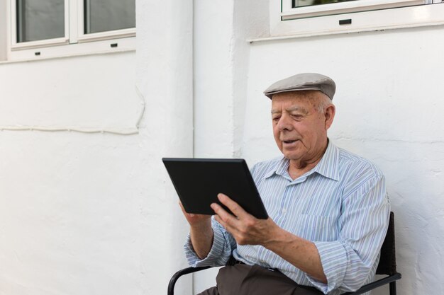 Älterer Mann benutzt eine Tablette im Yard seines Hauses