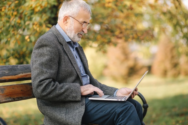 Älterer Mann benutzt Laptop im Park Schöner älterer Mann mit Brille arbeitet draußen