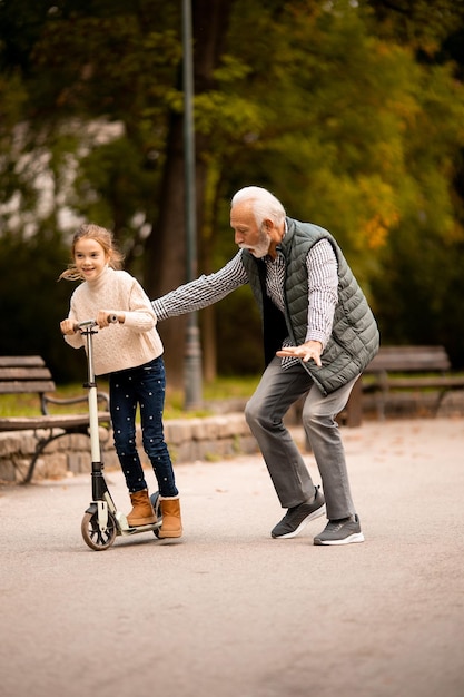 Älterer Mann bringt seiner Enkelin bei, wie man Tretroller im Park fährt