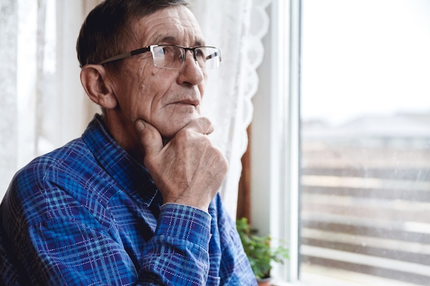 Älterer Mann, der am Fenster steht