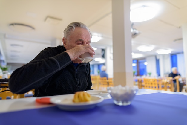 Älterer Mann, der an der Cafeteria im Pflegeheim isst