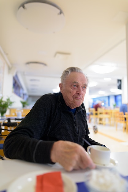 Älterer Mann, der an der Cafeteria im Pflegeheim isst