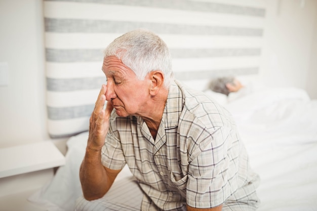 Älterer Mann, der auf Bett im Schlafzimmer sitzt