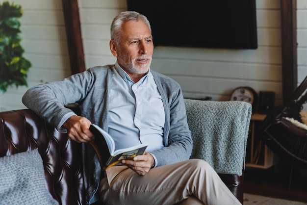 Älterer Mann, der auf Sofa sitzt und Buch liest