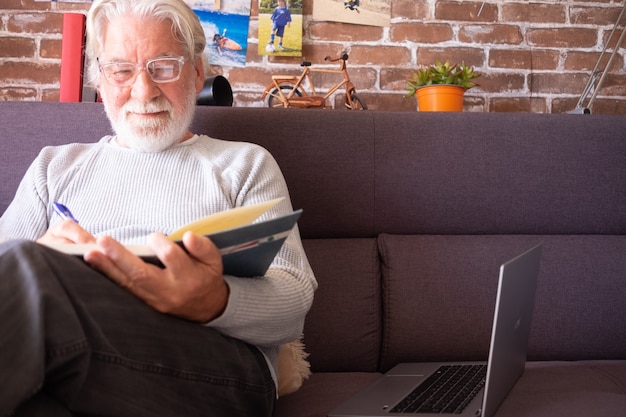 Älterer Mann, der auf Sofa sitzt und zu Hause ein Buch liest - Ruhestands-, Freizeit- und Menschenkonzept