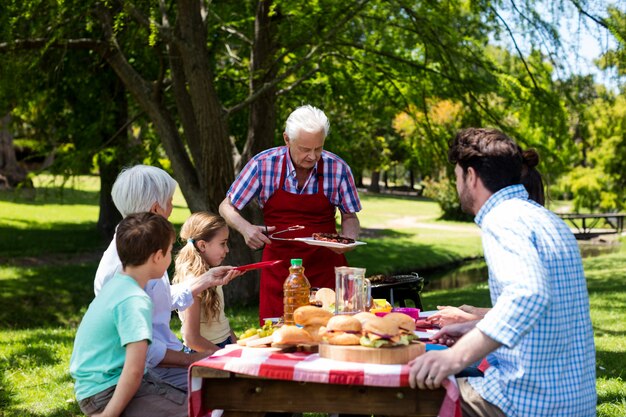 Älterer Mann, der der Familie im Park Grill dient