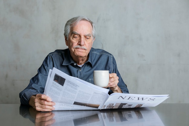 Älterer Mann, der die Nachrichten liest und Kaffee trinkt