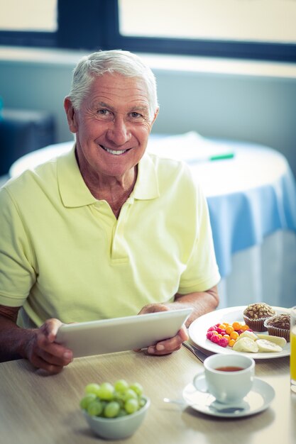 Älterer Mann, der digitale Tablette beim Frühstücken verwendet
