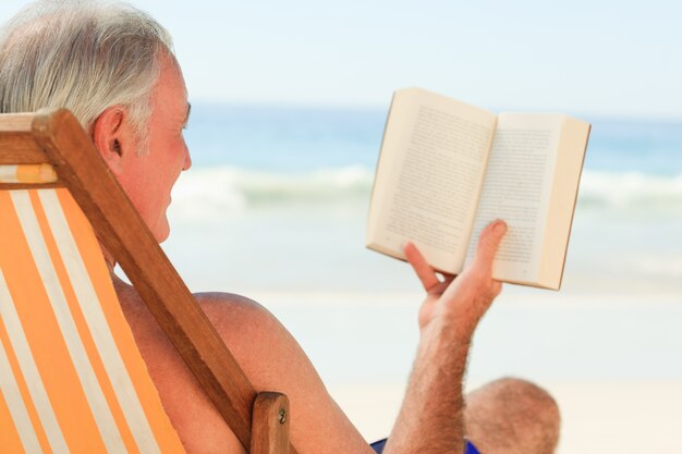 Älterer Mann, der ein Buch am Strand liest