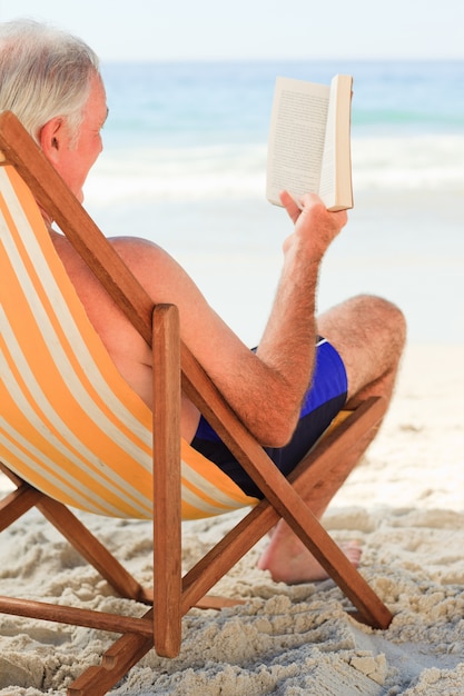 Älterer Mann, der ein Buch am Strand liest