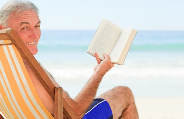 Älterer Mann, der ein Buch am Strand liest