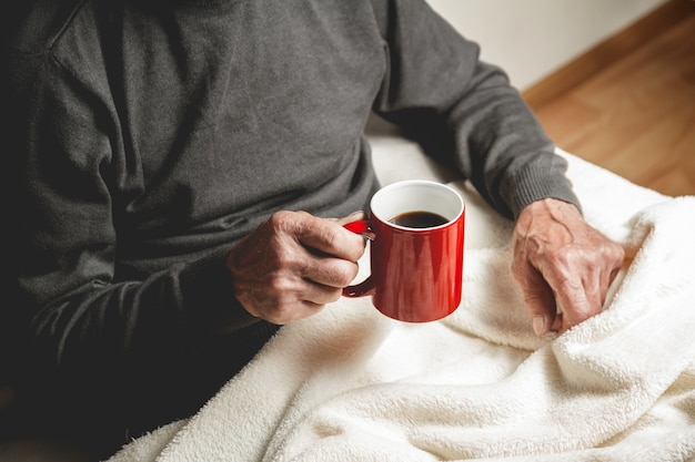 Älterer Mann, der mit einer Tasse Kaffee in der Hand sitzt