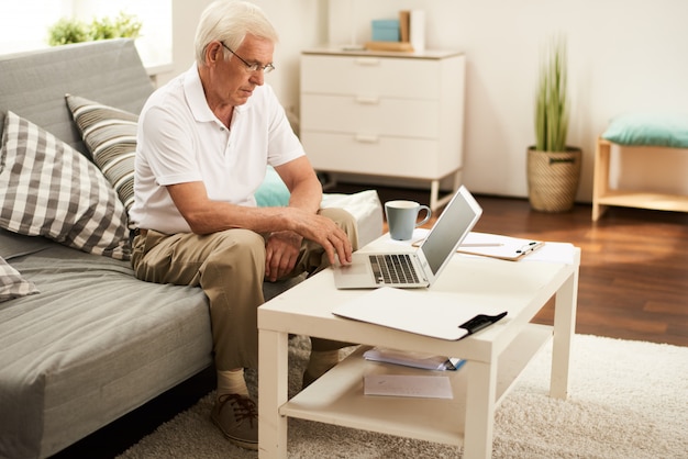 Älterer Mann, der mit Laptop zu Hause arbeitet