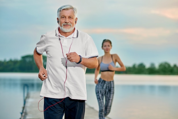 Älterer Mann, der Musik, laufend nahe See am Abend hört.