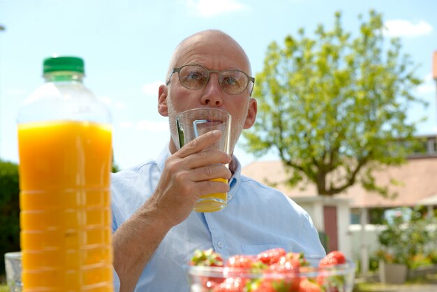 Älterer Mann, der Orangensaft in ihrem Garten trinkt