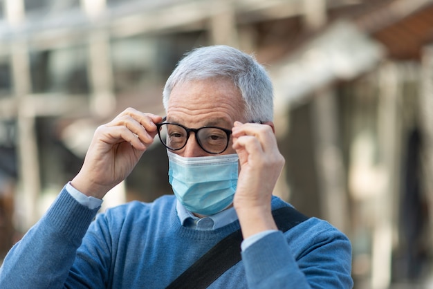 Älterer Mann, der seine Brille hält, beschlug aufgrund der Maske, Covid Coronavirus Vision Konzept