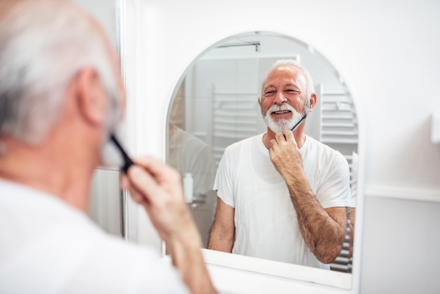 Älterer Mann, der seinen Bart putzt.