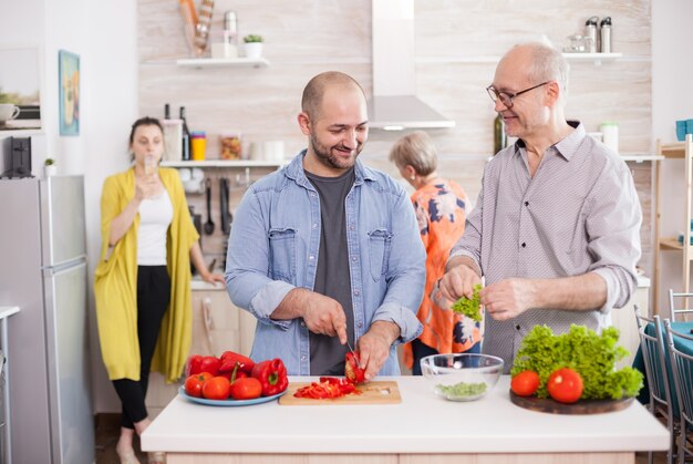 Älterer Mann, der Sohn anschaut, während er köstlichen Salat zubereitet.