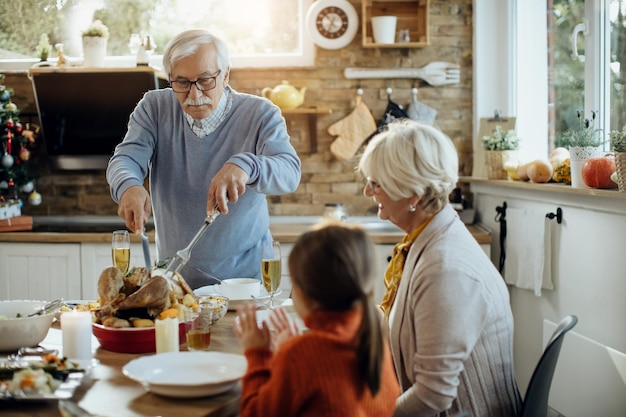 Älterer Mann, der während des Thanksgiving-Mittagessens zu Hause Truthahnfleisch schnitzt