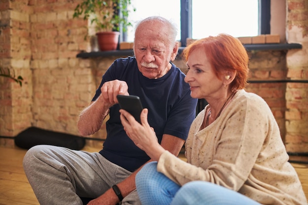 Älterer Mann, der während einer Diskussion mit einer reifen Frau auf den Smartphone-Bildschirm zeigt
