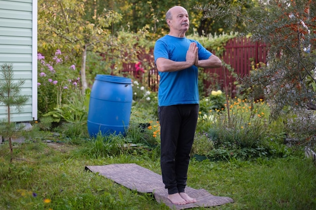Älterer Mann, der Yoga praktiziert, steht in Tadasana in seinem Garten
